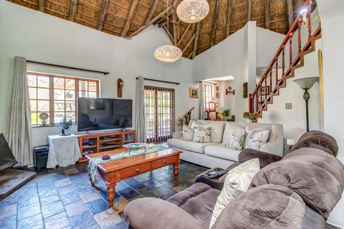 Spacious living room featuring a high vaulted thatched ceiling with exposed rafters, slate tile flooring, and a timber staircase leading to the upper level.