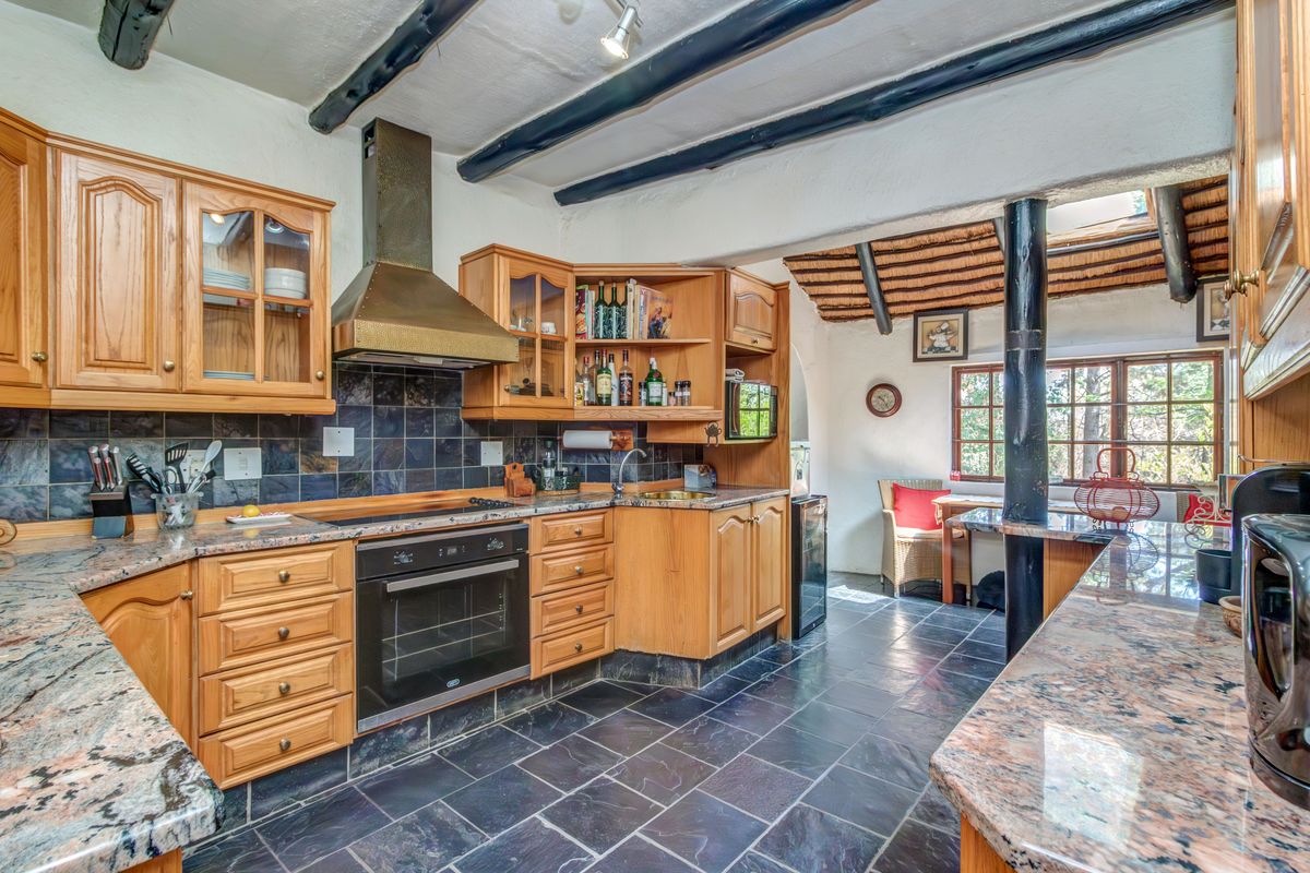A rustic kitchen featuring wooden cabinetry, granite countertops, slate flooring, and exposed timber ceiling beams, creating a warm and traditional atmosphere.