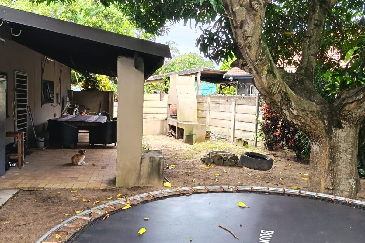 Rear garden area featuring a covered patio, built-in braai, and paved flooring, offering potential for outdoor entertainment space development.