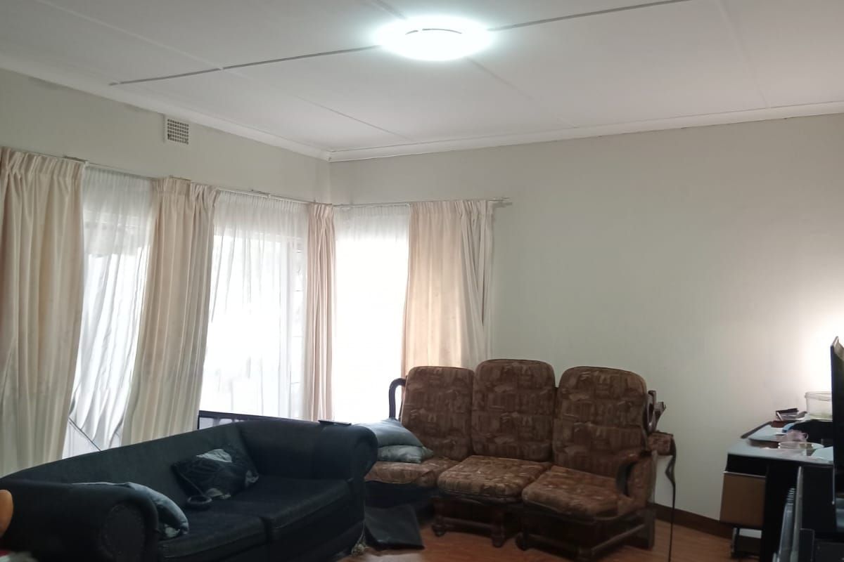 A living room featuring parquet flooring and a standard ceiling tile finish, offering a functional space with natural light from large windows.