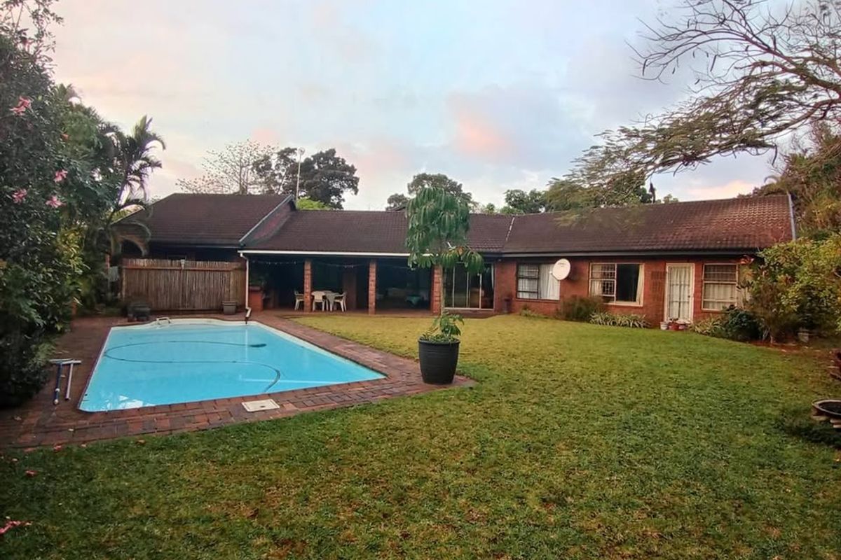 Rear view of the property featuring a swimming pool, a spacious lawn, and a covered patio area attached to the main house structure.
