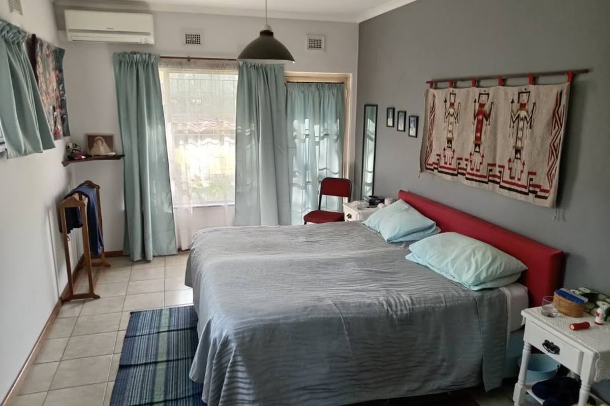 A functional bedroom featuring tiled flooring, a wall-mounted split-system air conditioner, and direct access to an outdoor area via a sliding glass door.
