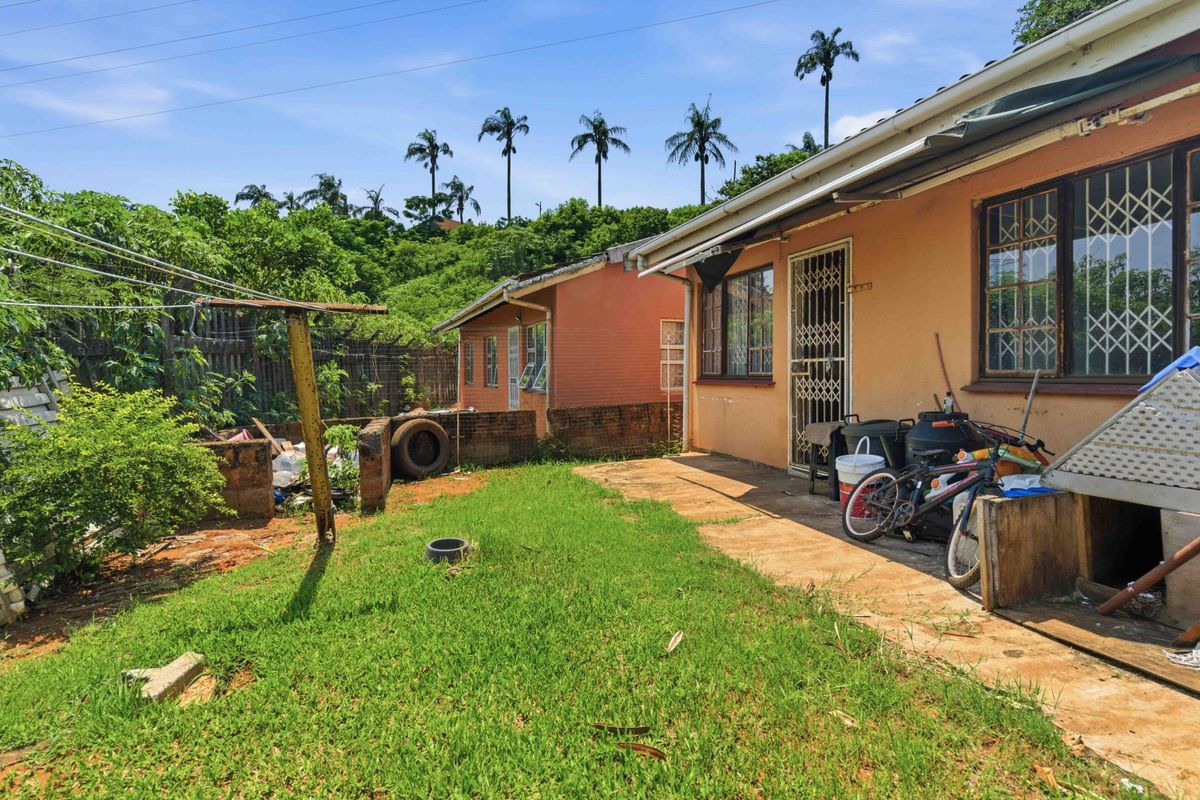 Rear exterior view of the townhouse featuring a small lawn, concrete patio area, and security gates on windows and doors.