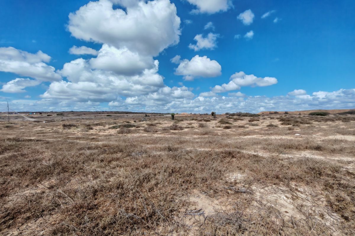 An expansive, undeveloped plot of vacant residential land featuring natural scrub vegetation under a clear blue sky.