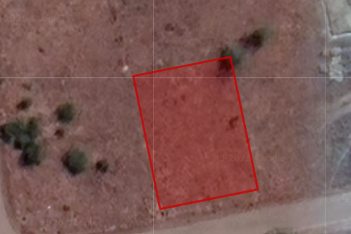 An aerial view of a vacant residential plot of land, highlighted in red, showing the surrounding terrain and access roads.
