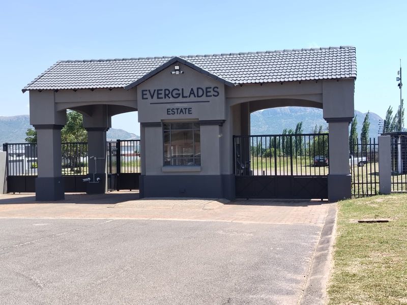 The main entrance gatehouse of Everglades Estate, featuring a secure guardhouse, paved driveway, and metal security gates.