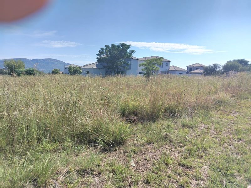 A view of a vacant residential plot featuring natural grass coverage with surrounding residential development and mountain views in the distance.