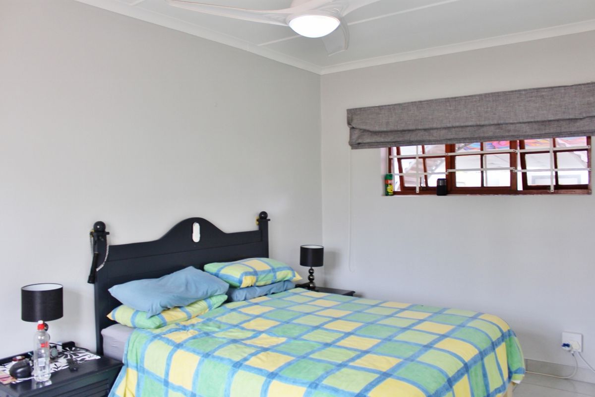 A bedroom featuring a ceiling fan, timber-framed window with security bars, and neutral wall finishes.