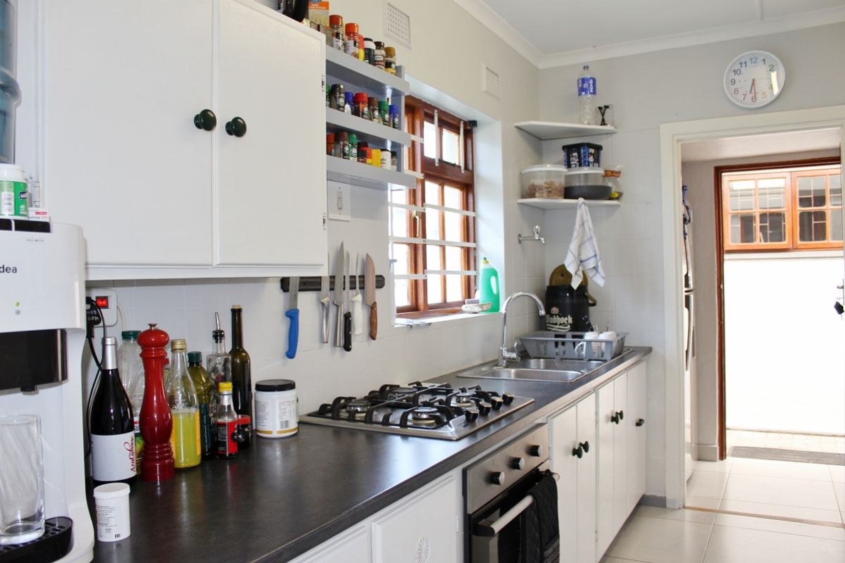 Functional kitchen featuring white cabinetry, dark laminate countertops, a gas hob, built-in oven, and a stainless steel sink with tiled splashback.