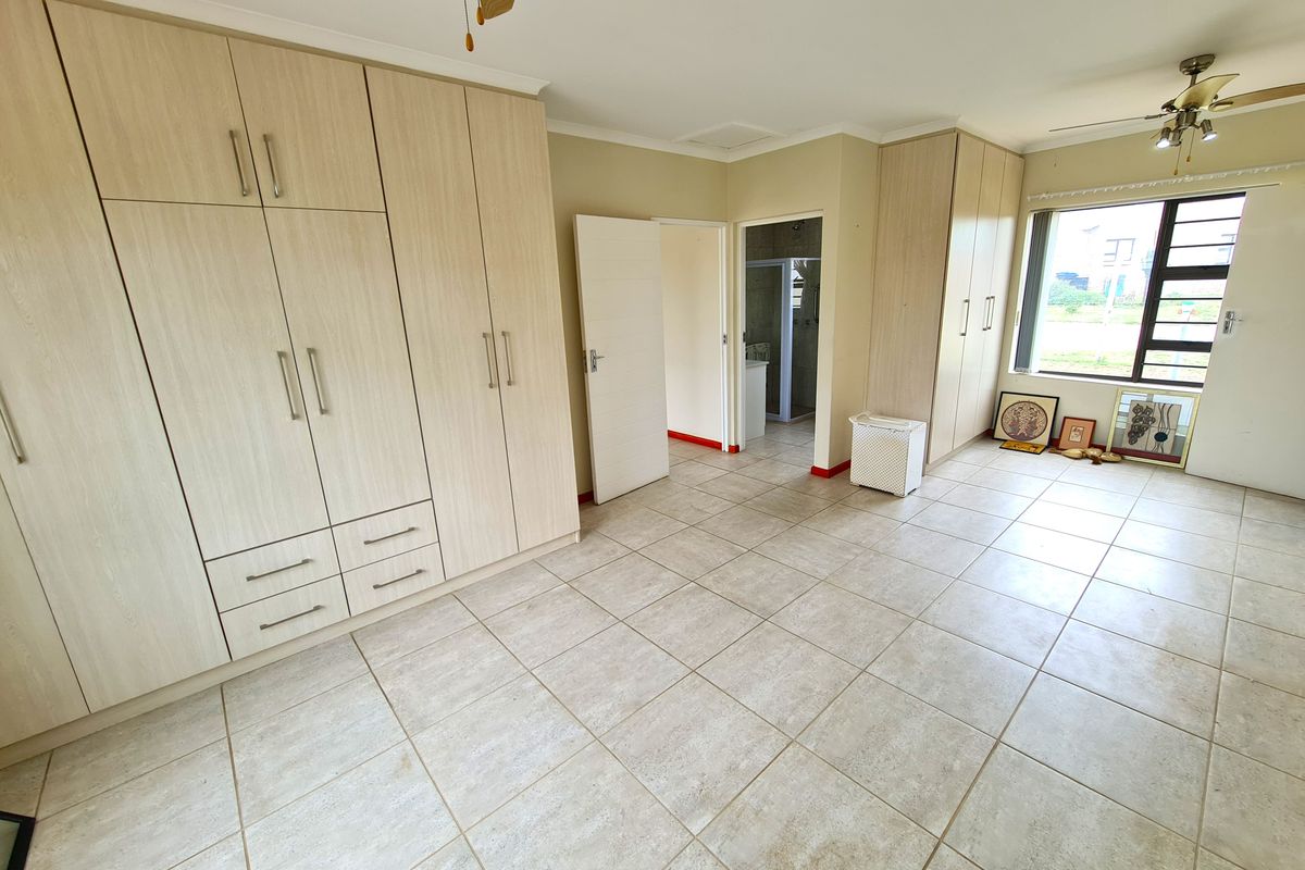 Spacious bedroom featuring extensive built-in cupboards, neutral tiled flooring, and a ceiling fan, with an adjoining en-suite bathroom.