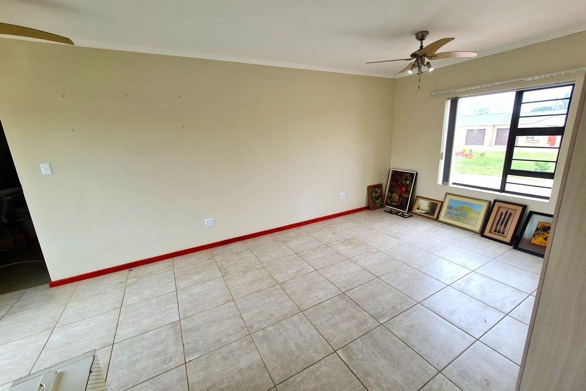 A spacious, empty living room featuring neutral tiled flooring, a ceiling fan, and large windows providing natural light.