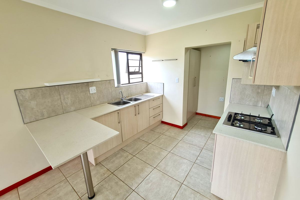 A functional kitchen featuring light wood cabinetry, gas hob, extractor fan, tiled flooring, and a dedicated pantry area with neutral wall finishes.