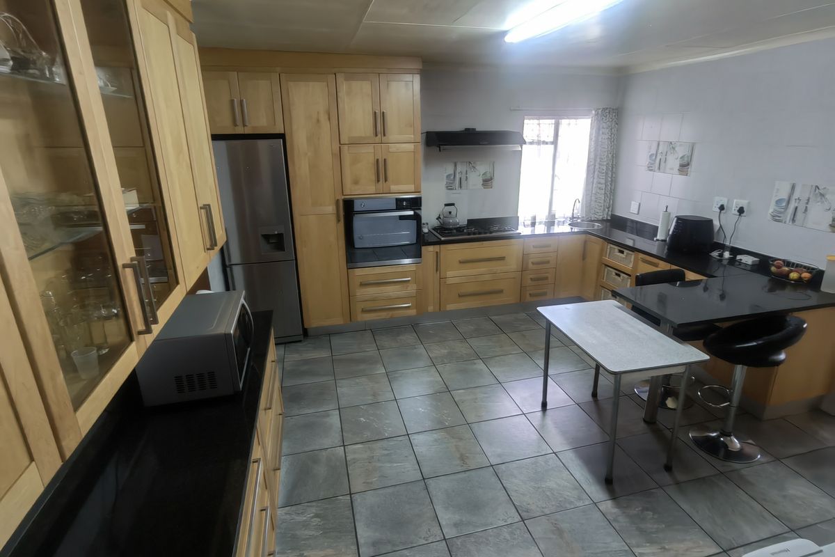A functional kitchen featuring light wood cabinetry, granite countertops, built-in oven, gas hob, and tiled flooring with a breakfast nook area.