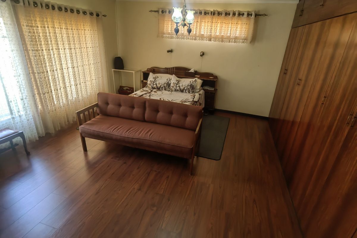 Spacious bedroom featuring extensive built-in wooden cabinetry, laminate flooring, and large windows with curtain rails.
