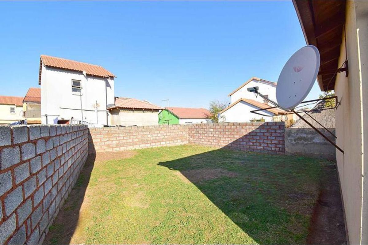 A rear garden area featuring a lawn enclosed by perimeter brick boundary walls and a satellite dish mounted to the exterior wall.