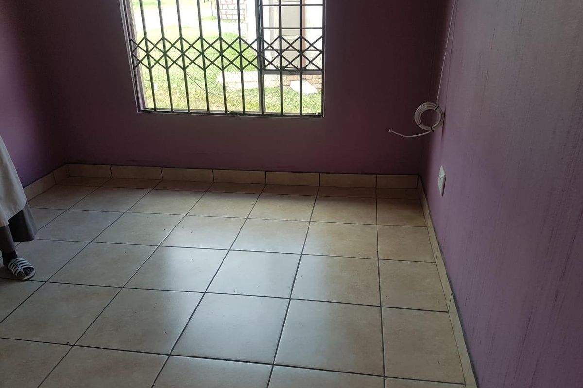 A vacant bedroom featuring tiled flooring, purple painted walls, and a window fitted with security bars.