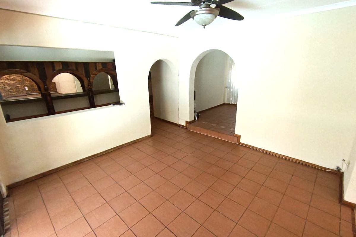 An empty living area featuring terracotta floor tiles, a ceiling fan, and distinctive arched doorways leading to adjacent rooms.