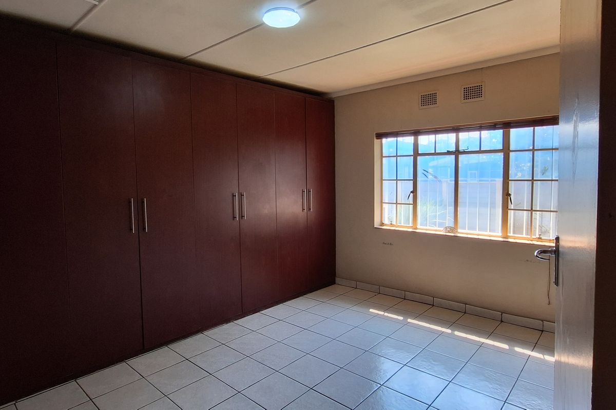 A bedroom featuring extensive built-in wooden cabinetry, tiled flooring, and a window with security bars.