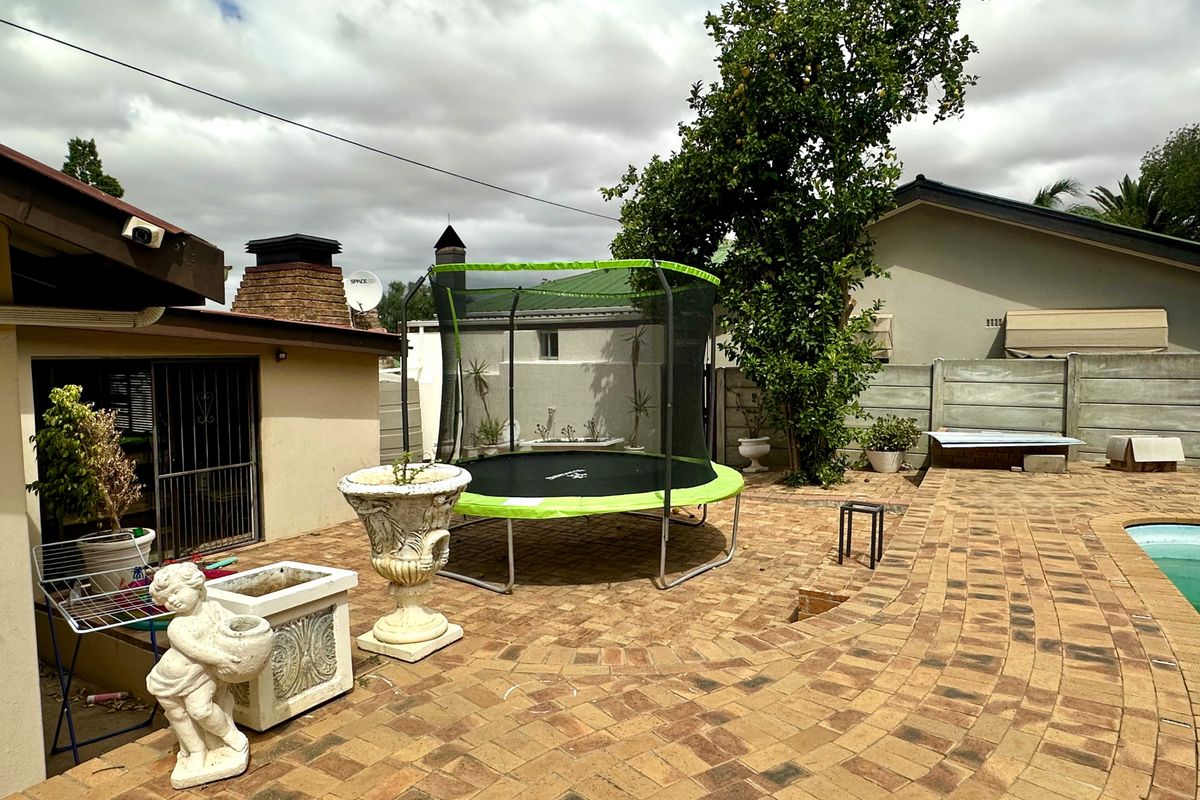 A paved rear courtyard area featuring a brick chimney stack, perimeter walling, and access to the pool area.