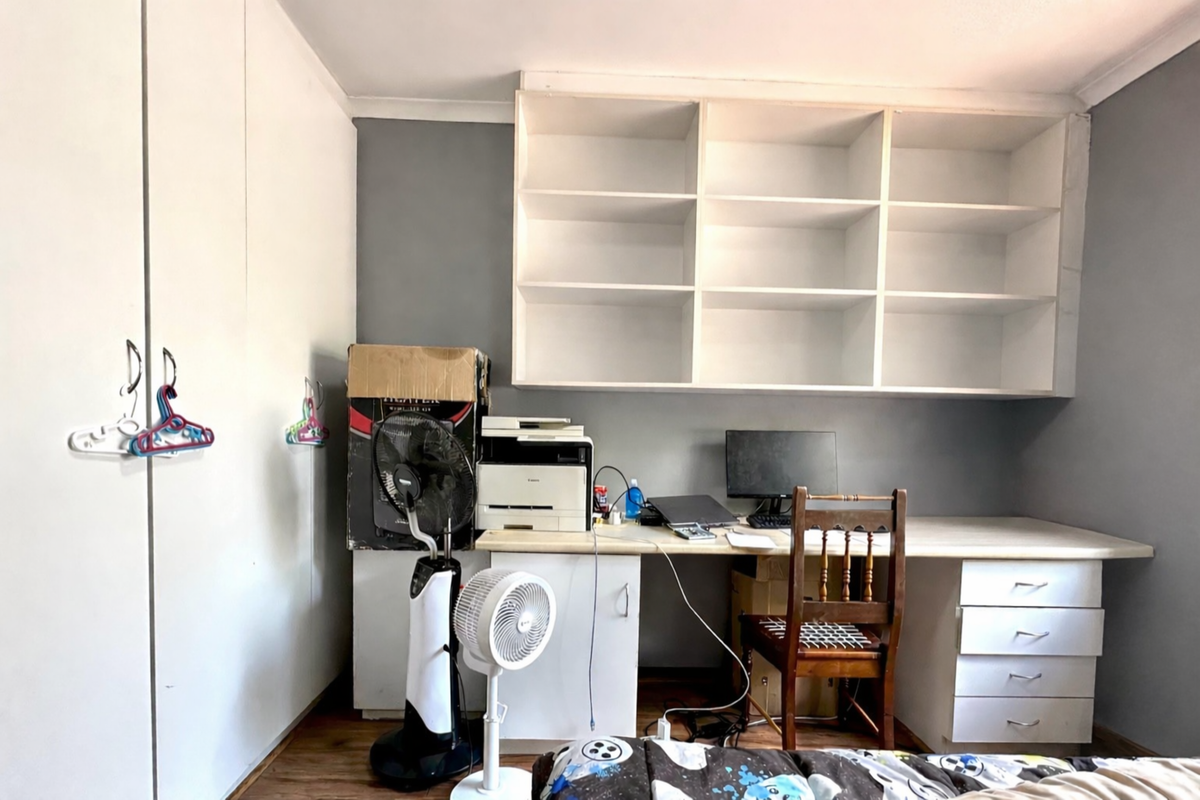A bedroom featuring built-in floor-to-ceiling wardrobes and a dedicated study nook with integrated shelving and desk drawers.