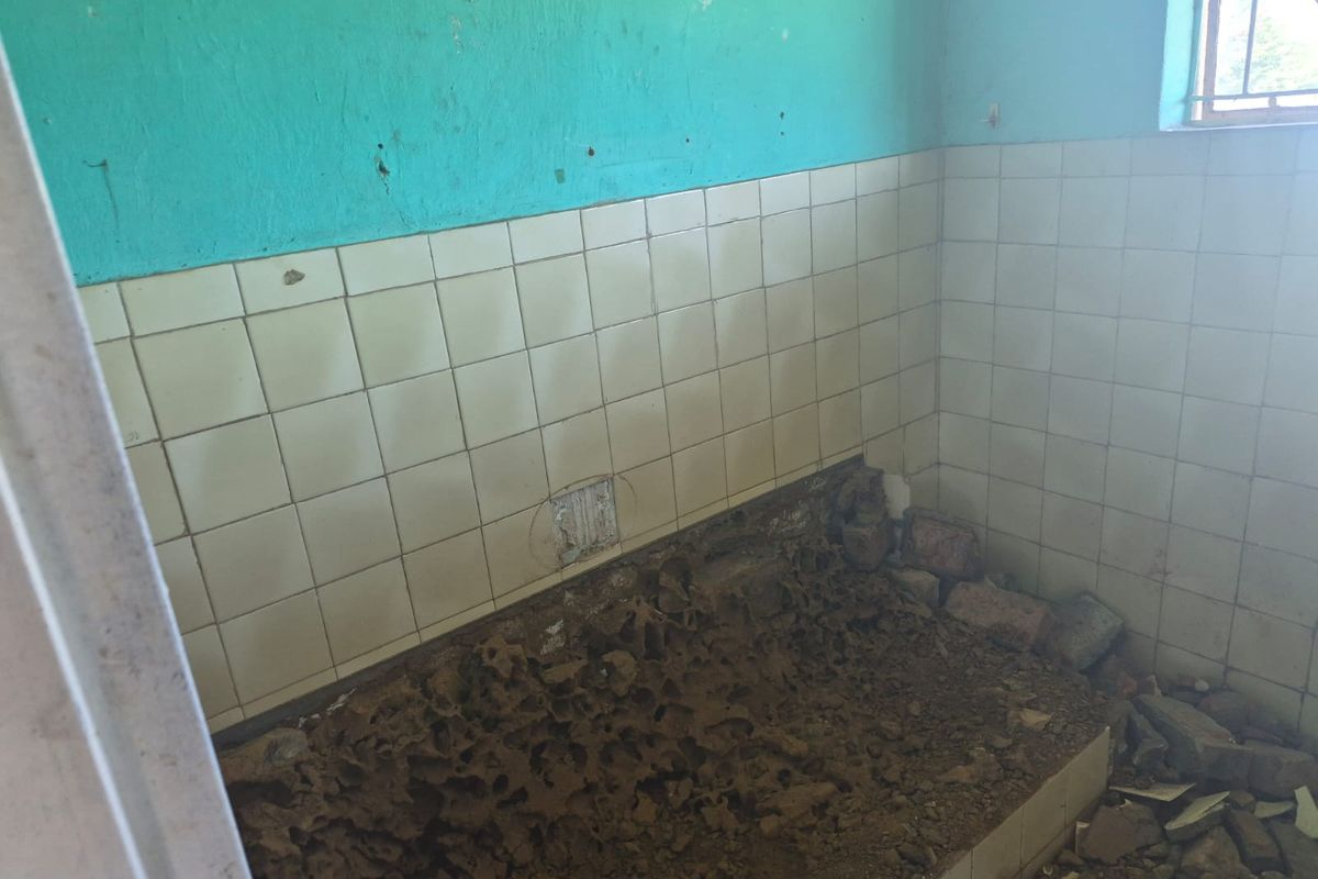 A severely dilapidated bathroom space requiring complete renovation, featuring damaged wall tiles and significant structural debris on the floor.