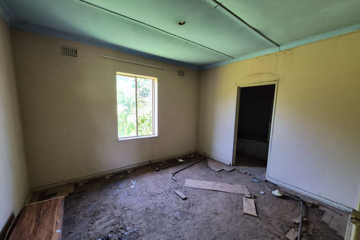 An empty bedroom requiring significant renovation, featuring exposed subflooring, damaged wall finishes, and basic window infrastructure.