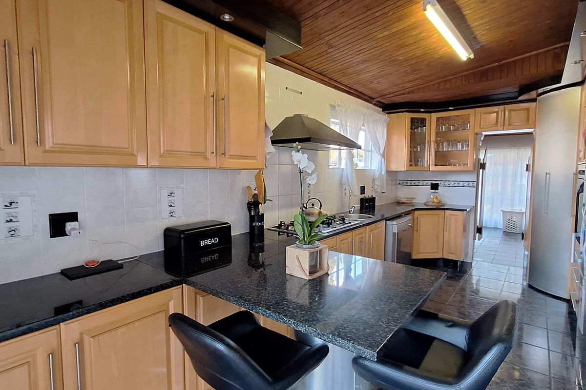 A functional kitchen featuring light wood cabinetry, dark granite countertops, a breakfast bar, and a distinctive wood-paneled ceiling with integrated lighting.