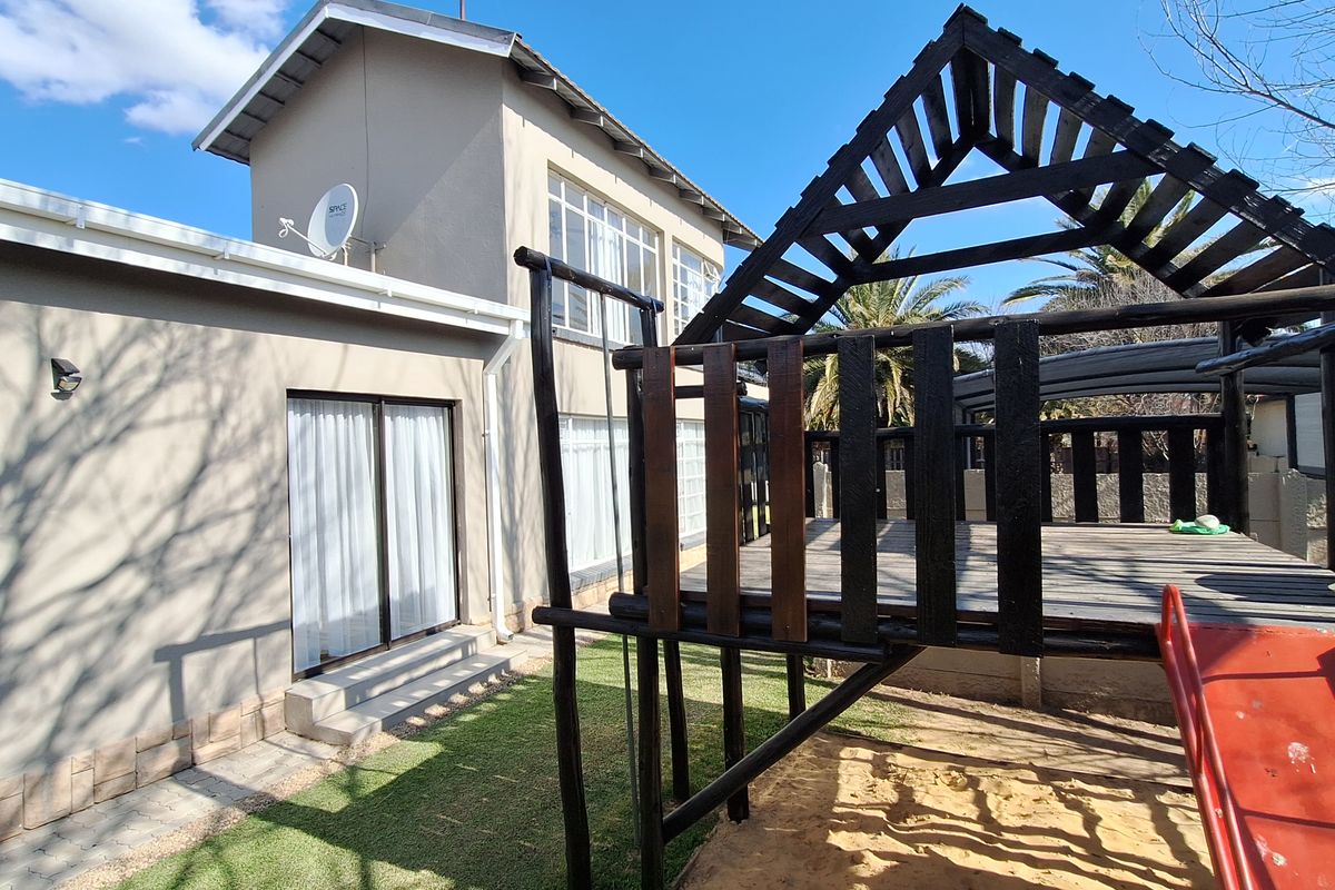 Rear view of the property featuring a multi-story building facade, sliding glass doors, and a wooden play structure in the garden area.