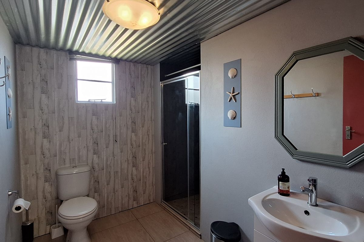 A functional bathroom featuring a vanity with basin, a toilet, and a glass-enclosed shower, finished with tiled flooring and a corrugated metal ceiling.