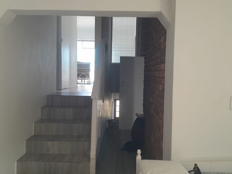 A hallway featuring a staircase with tiled steps, a decorative exposed brick wall, and a white balustrade leading to an adjacent living area.