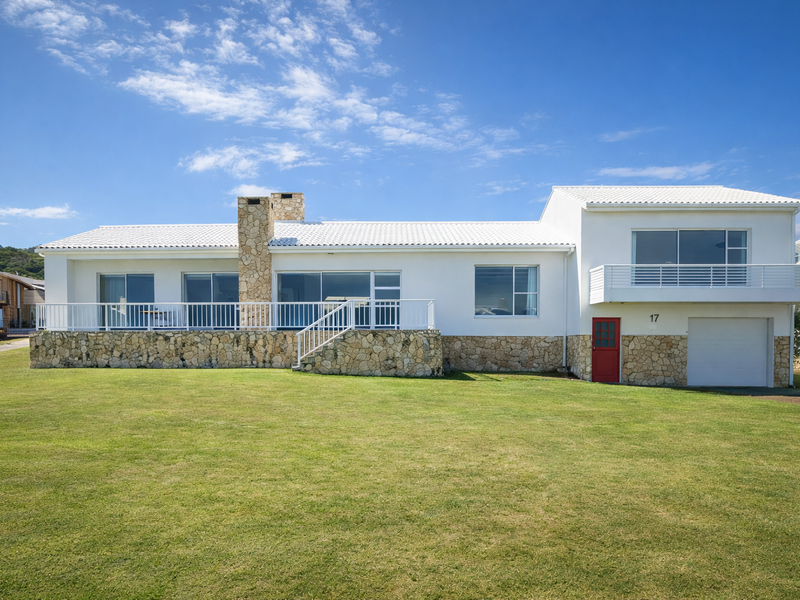 A well-maintained two-story house featuring stone cladding, a white tiled roof, a spacious balcony, and a garage, set against a large lawn.