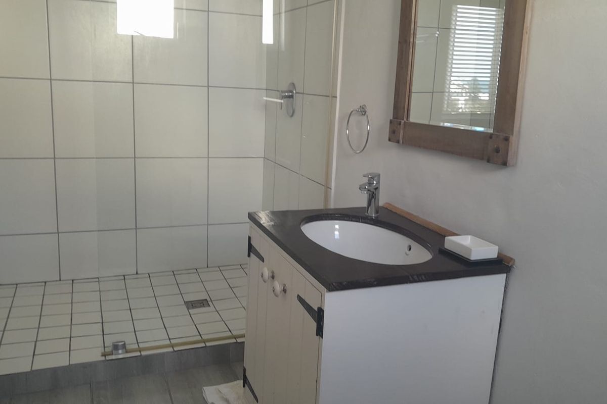 A functional bathroom featuring a walk-in shower with tiled walls and a vanity unit with a basin and mirror.