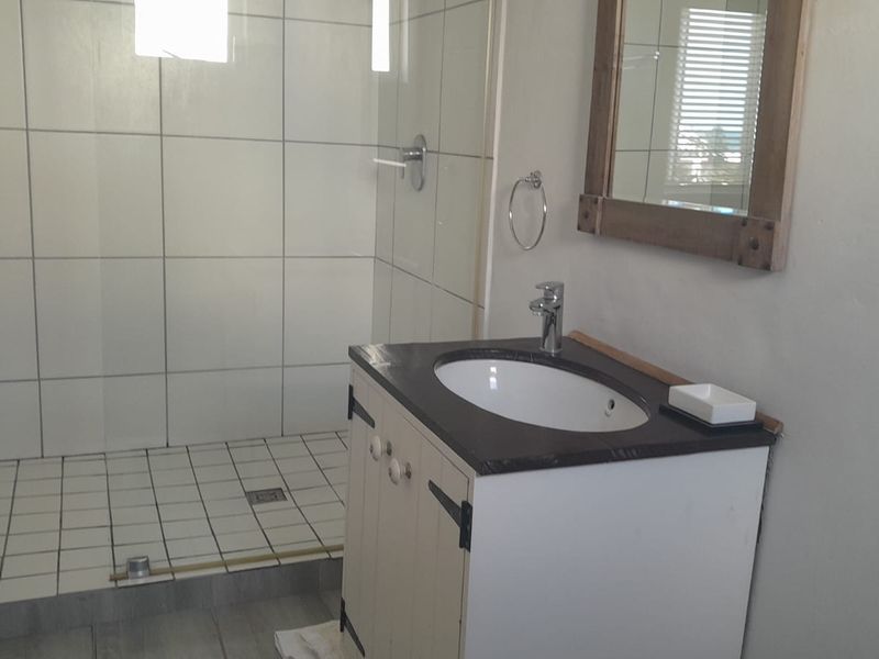 A functional bathroom featuring a walk-in shower with tiled walls and a vanity unit with a basin and mirror.