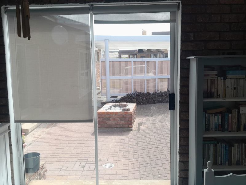 View from an interior living space looking out onto a paved patio area featuring a built-in brick braai and enclosed garden space.