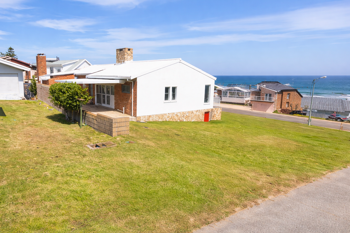 Rear view of the property featuring a stone chimney, metal roof, and stone base cladding, set on a sloped lawn with ocean views.