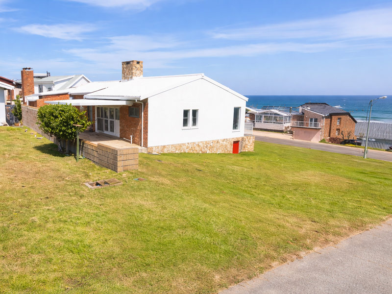 Rear view of the property featuring a stone chimney, metal roof, and stone base cladding, set on a sloped lawn with ocean views.