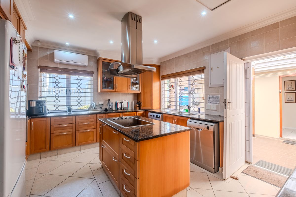 A functional kitchen featuring wooden cabinetry, granite countertops, a central island with a built-in hob, and a stainless steel extractor fan.
