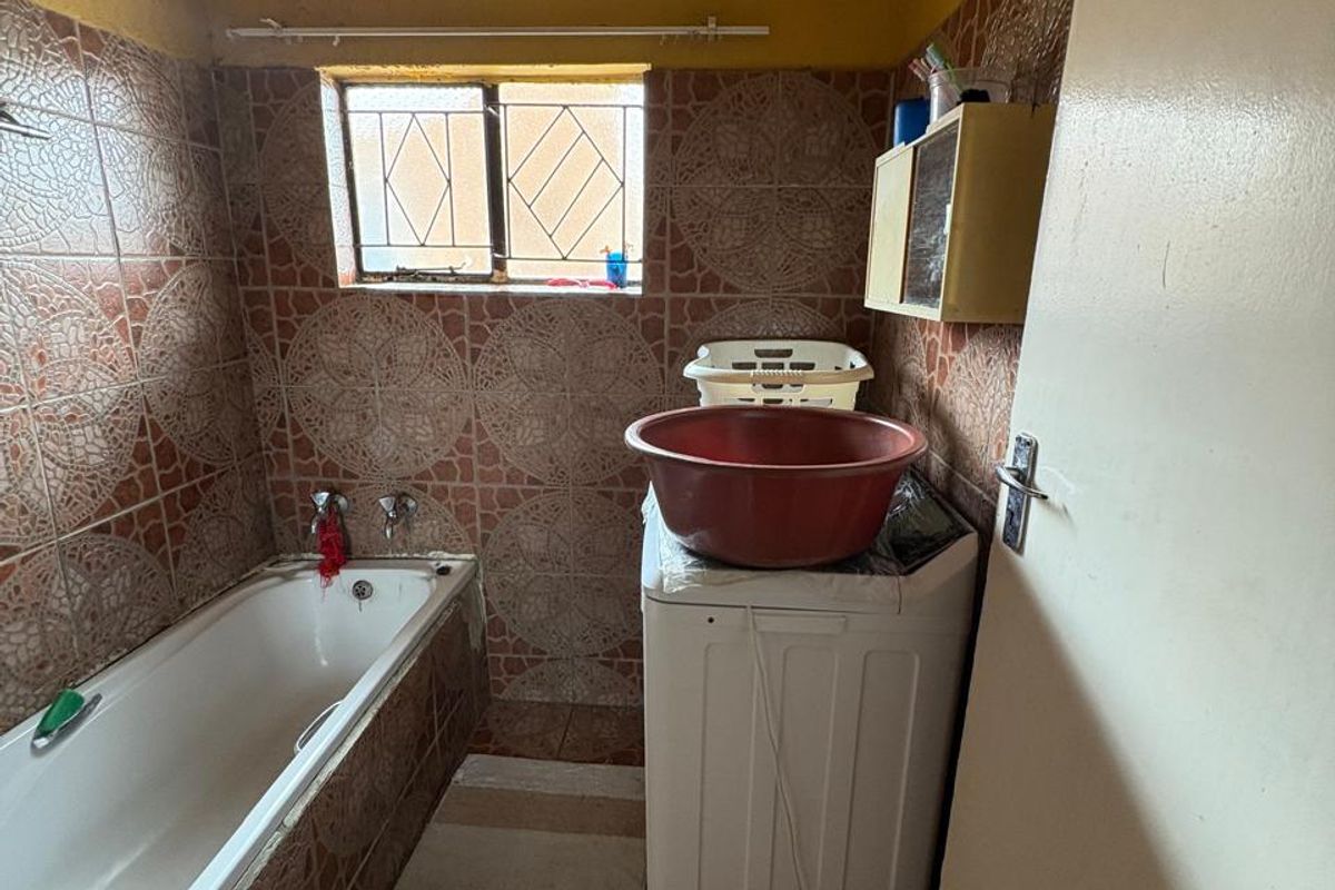 A functional bathroom featuring a built-in bathtub, tiled walls and flooring, and space for laundry appliances.