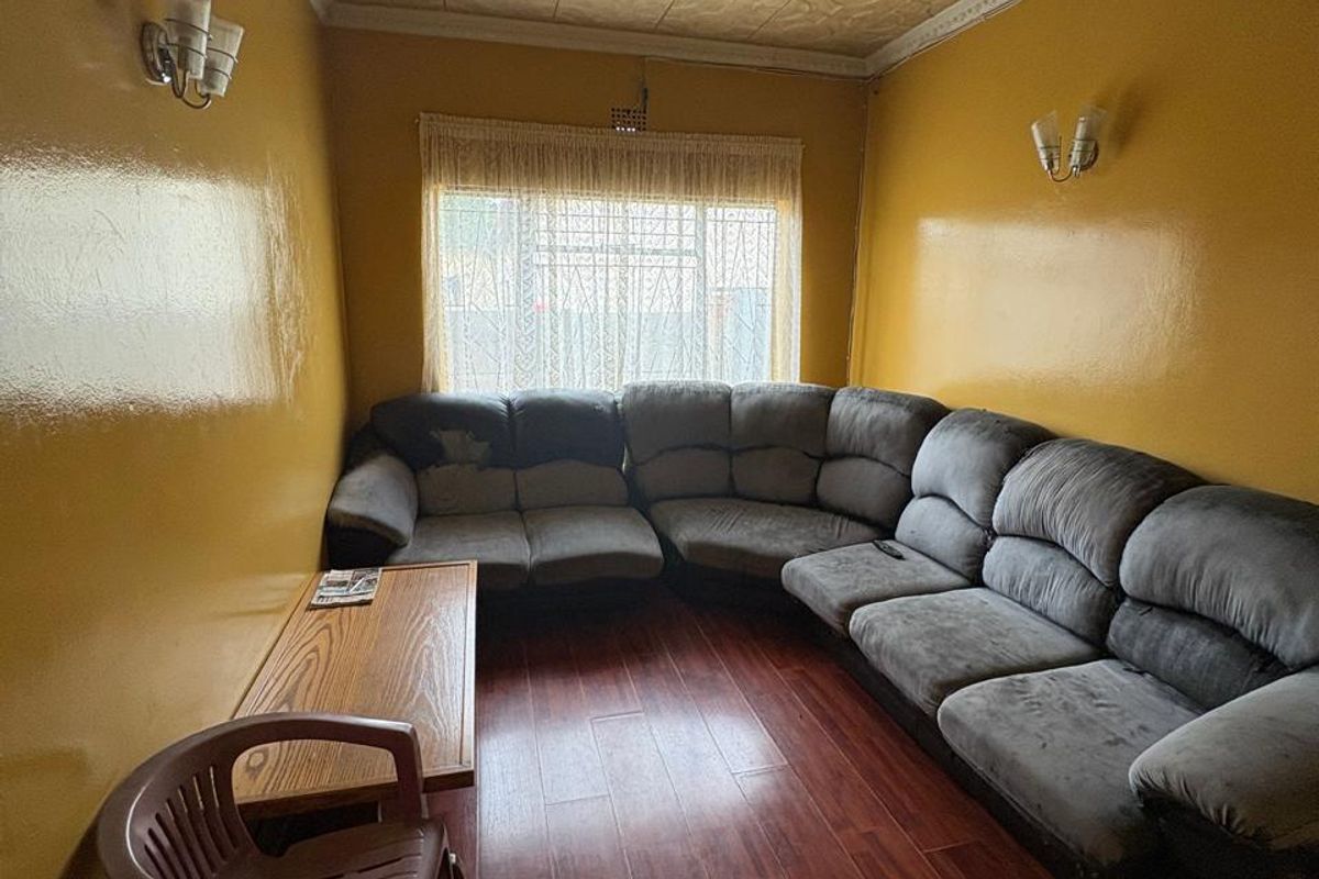 A living room featuring dark wood-look flooring, yellow painted walls, and a decorative textured ceiling with wall-mounted light fixtures.