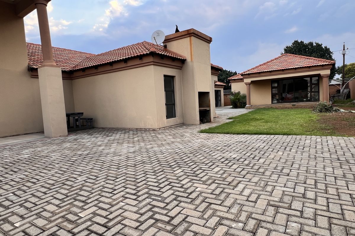 Rear exterior view of the house featuring a paved courtyard, built-in braai area, and a separate outbuilding structure with a tiled roof.