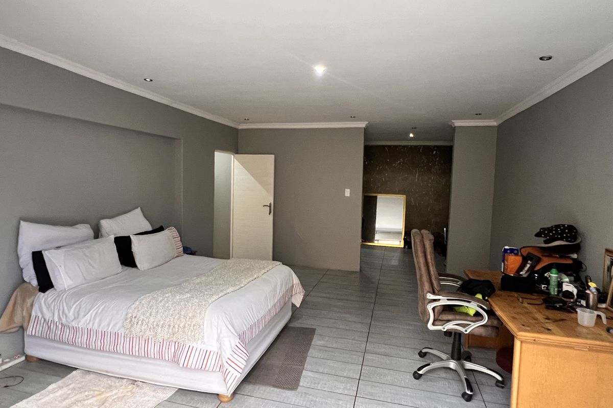 Spacious bedroom featuring tiled flooring, recessed ceiling lighting, and a neutral color palette, offering a versatile layout for sleeping and workspace areas.