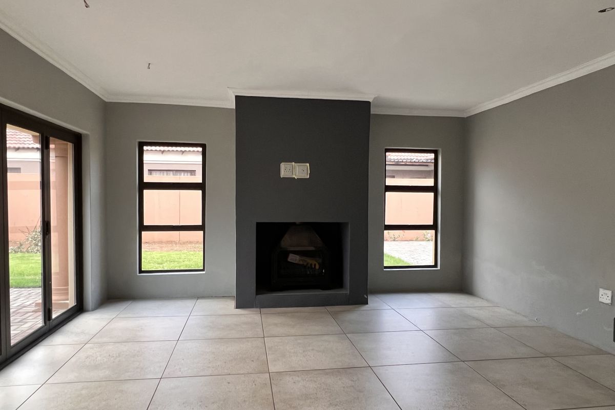 A spacious, empty living room featuring large ceramic floor tiles, a central dark-toned fireplace, and sliding glass doors leading to the exterior.