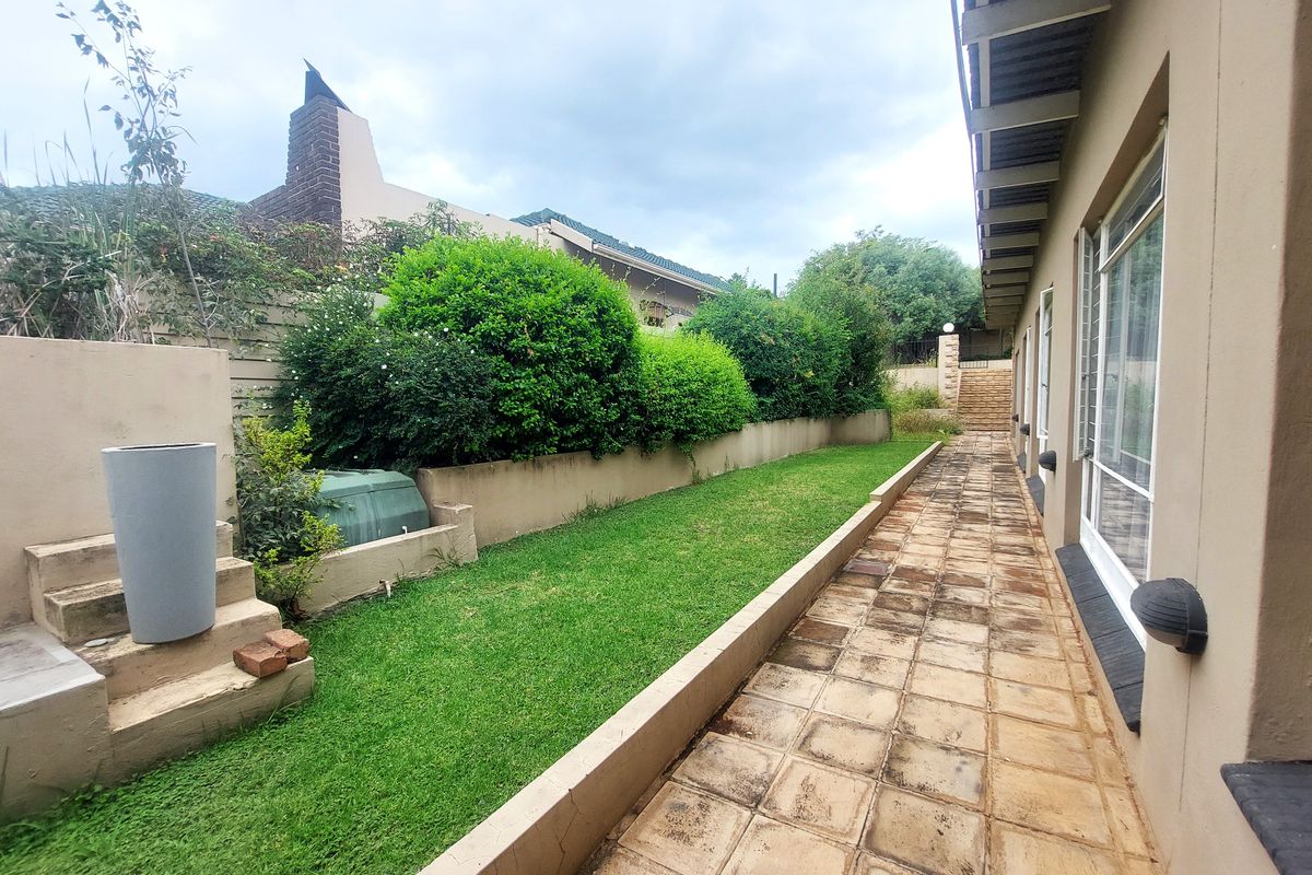 A rear exterior view featuring a paved walkway alongside a lawn, retaining walls, and established garden greenery.