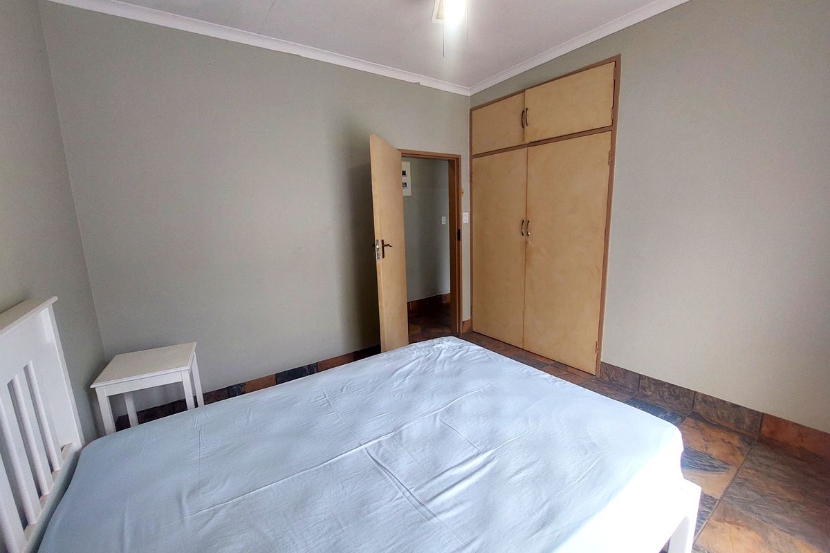A functional bedroom featuring built-in wooden cupboards, tiled flooring, and a ceiling fan, offering a neutral base for potential interior updates.
