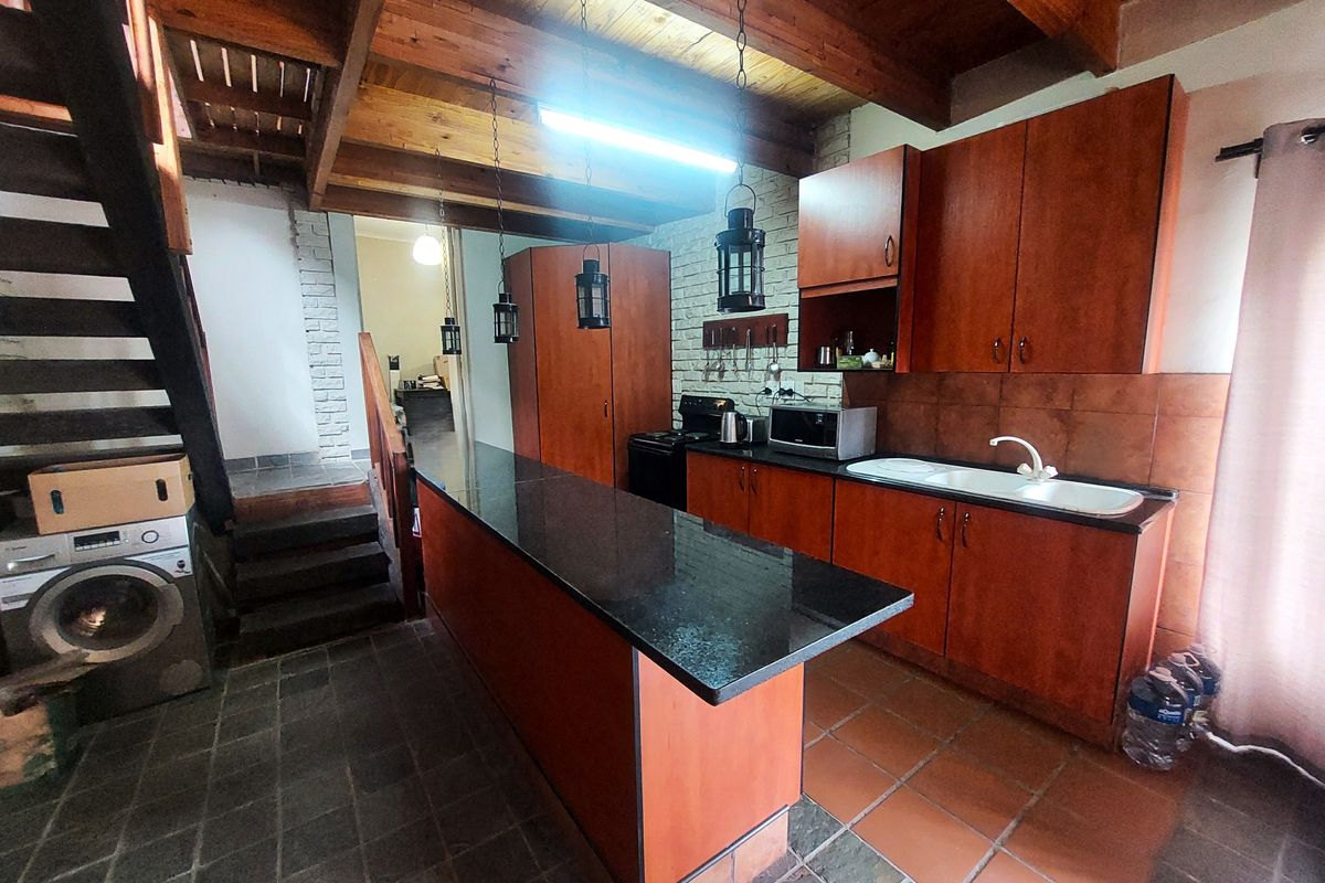 Kitchen featuring exposed timber beams, granite breakfast bar, built-in wooden cabinetry, and tiled flooring, with an adjacent staircase leading to an upper level.