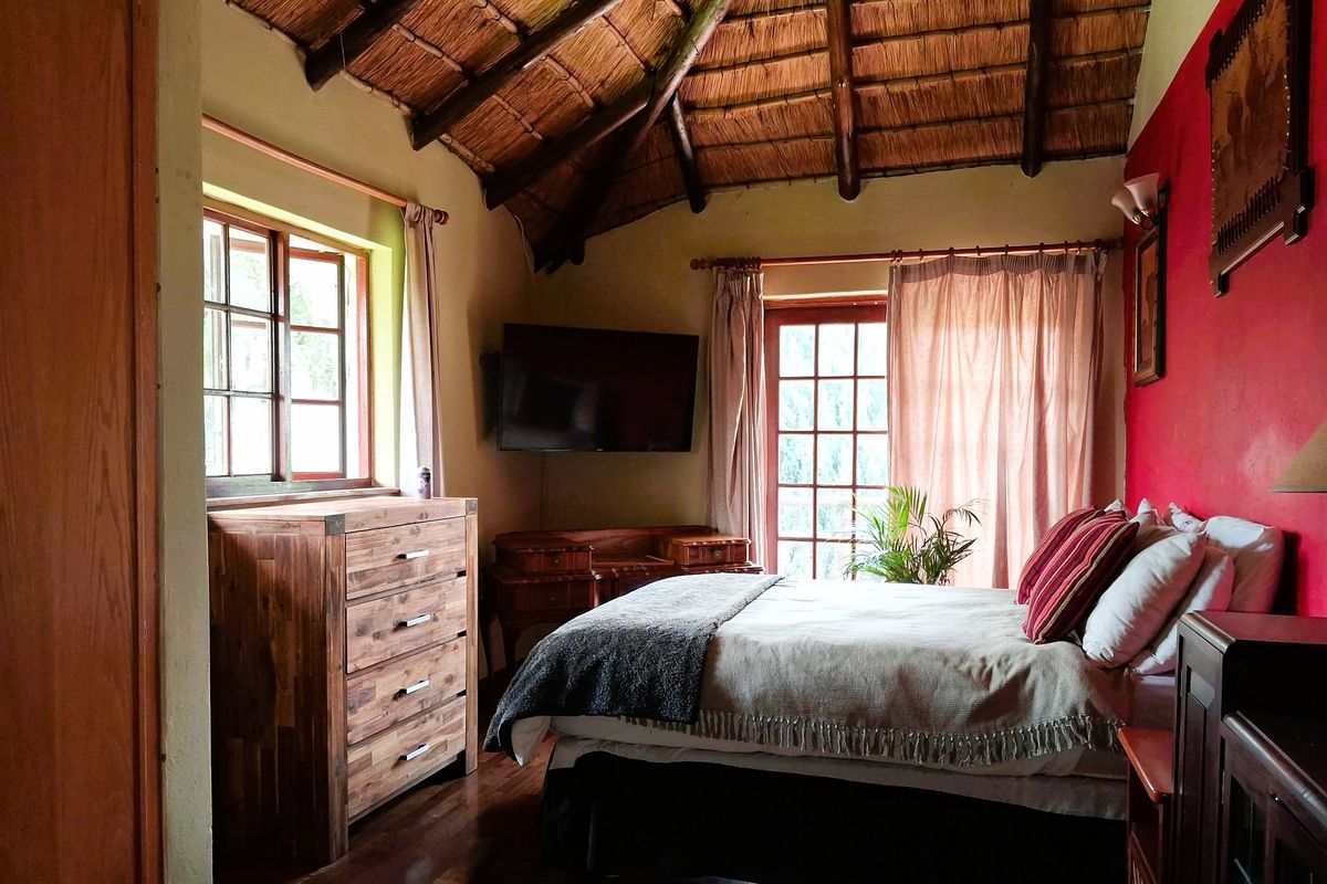 A cozy bedroom featuring a traditional exposed thatch ceiling, hardwood flooring, and natural light through timber-framed windows and doors.