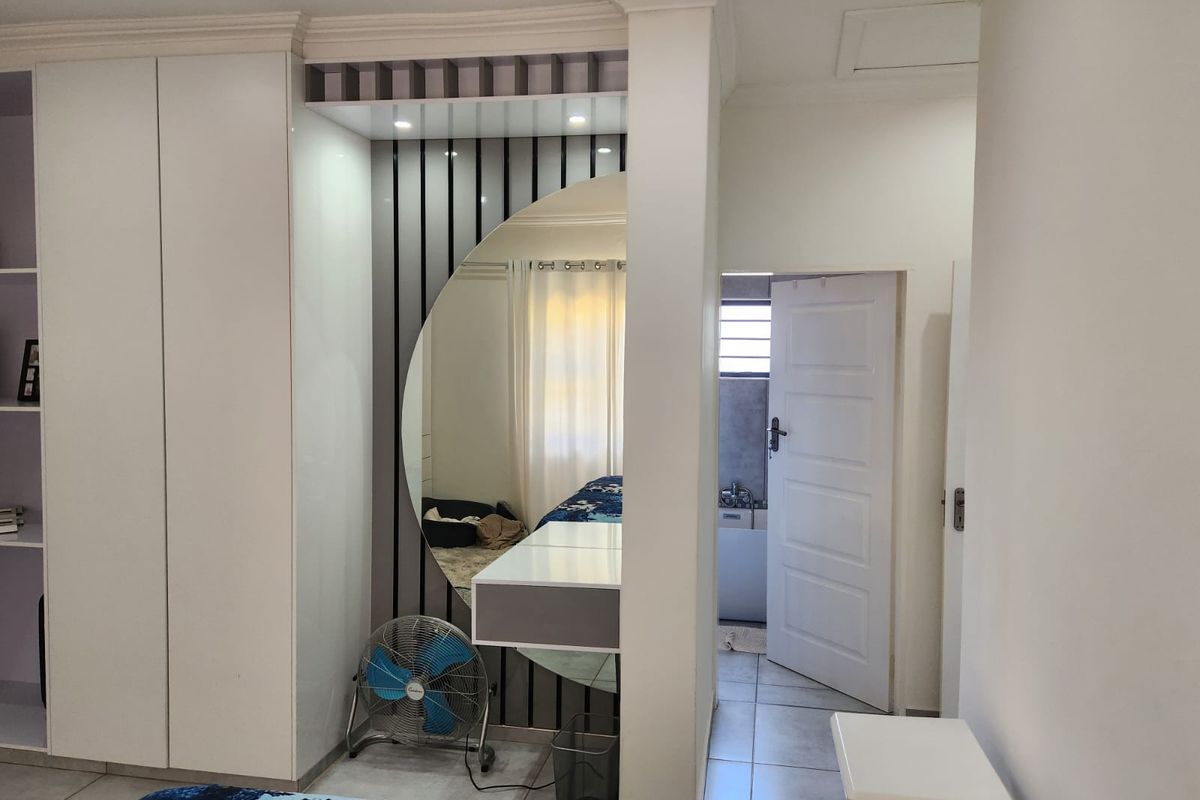 A well-maintained bedroom featuring built-in cupboards, a modern vanity area with a large circular mirror, and direct access to an en-suite bathroom.