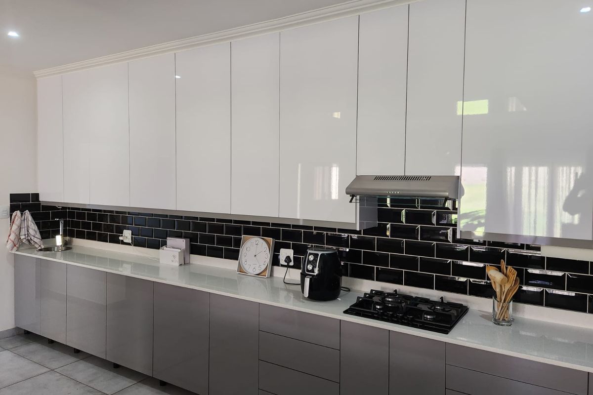 Modern kitchen featuring high-gloss cabinetry, a contrasting black subway tile backsplash, stone countertops, and integrated gas hob with extractor fan.