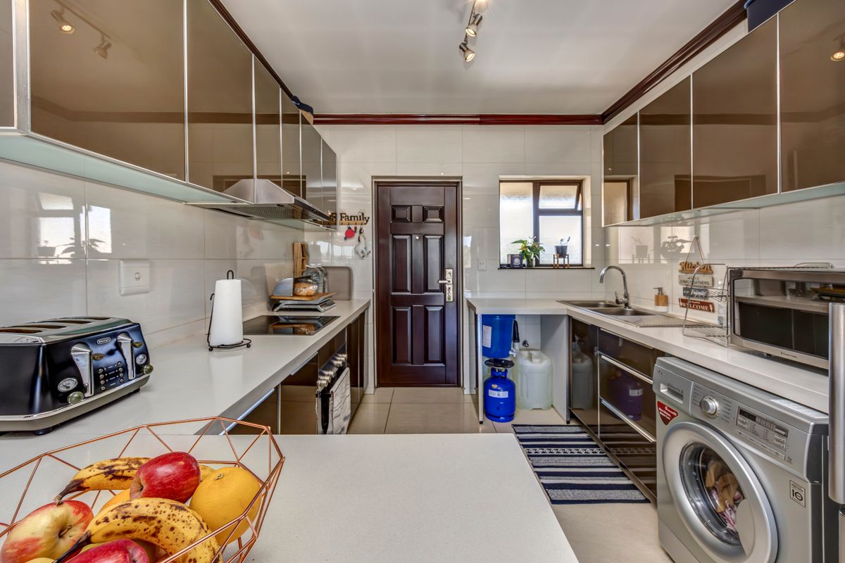 Modern galley-style kitchen featuring high-gloss cabinetry, stone countertops, integrated hob, and tiled finishes, providing a functional and well-maintained cooking space.