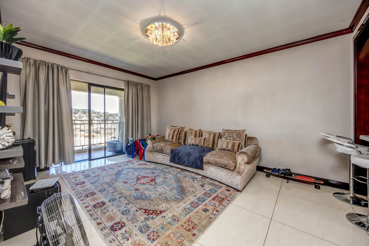 A living room featuring large format floor tiles, crown molding, and a sliding glass door providing access to an outdoor balcony area.